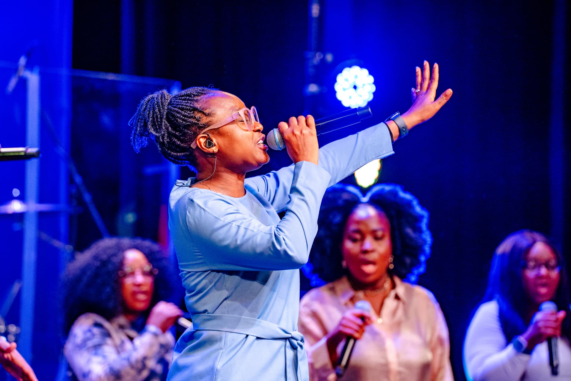 A worship leader singing with one hand raised during Glorious Praise